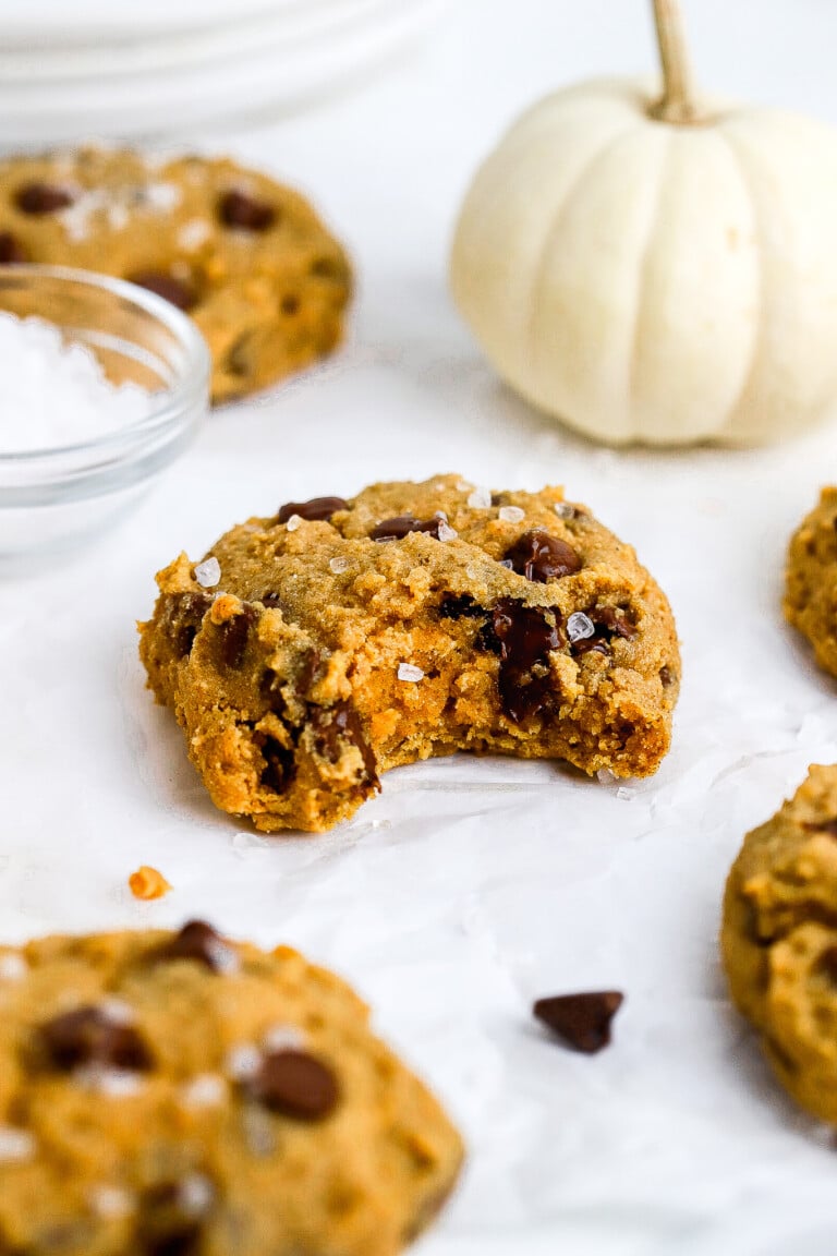 Side angle of gluten free pumpkin cookies on parchment paper with mini white pumpkin in background.