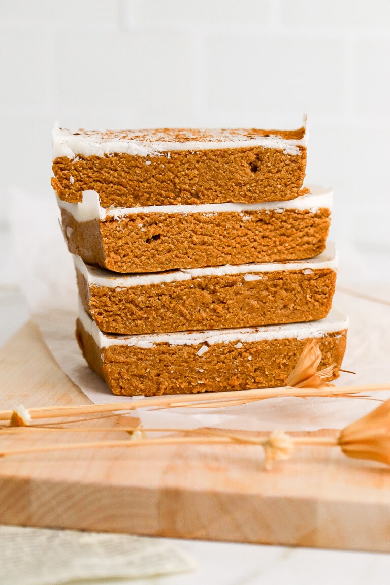 Side angle of homemade pumpkin protein bars stacked on top of one another with a white chocolate topping.