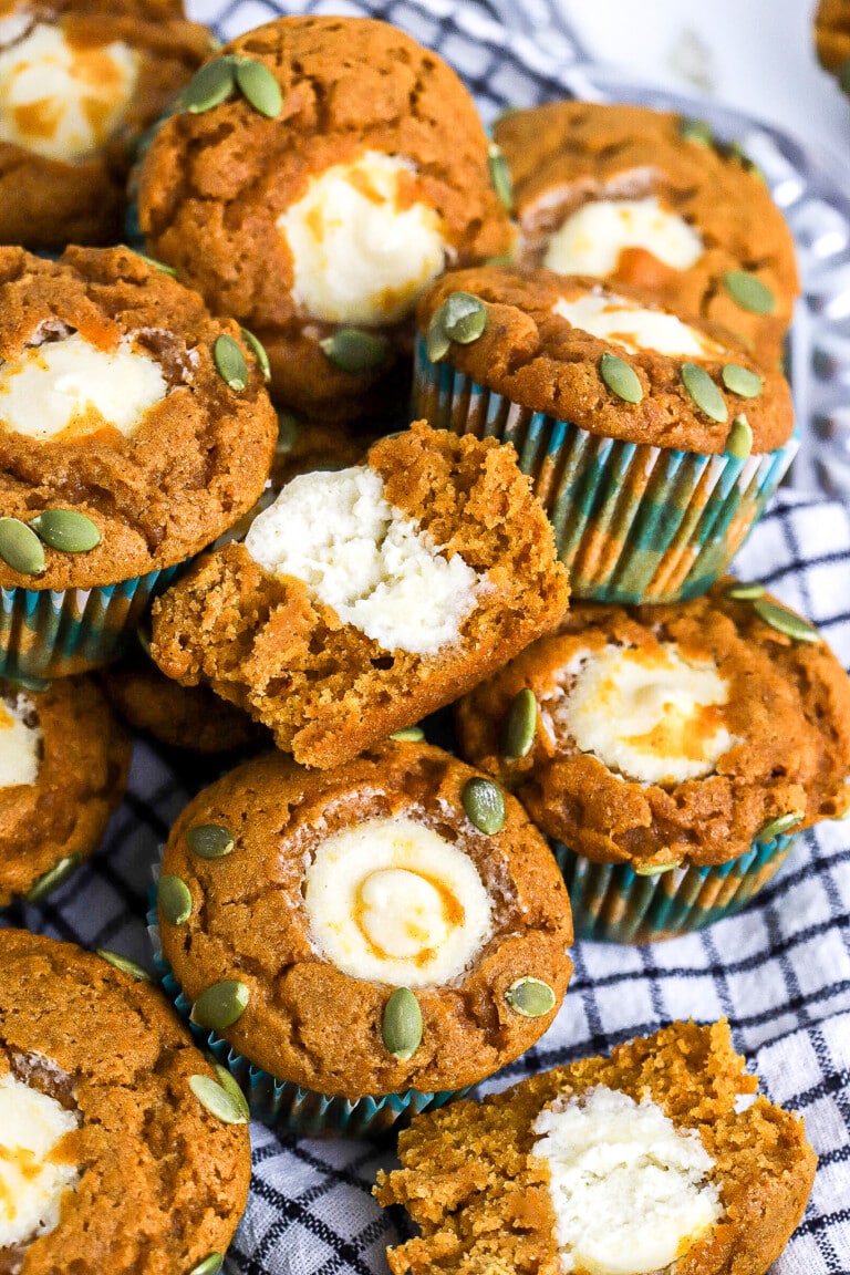 Side view of a half of a pumpkin muffin with cream cheese filling in the centre with pumpkin seeds on top.