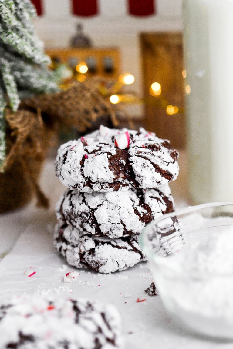 Side view of gluten free chocolate crinkle cookies stacked on top of one another with twinkle lights in background.