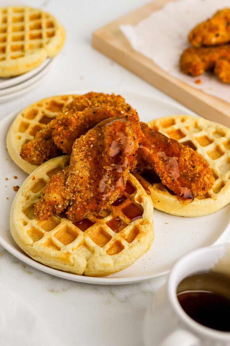 Side angle of homemade air fryer chicken and waffles on white plate with maple syrup.