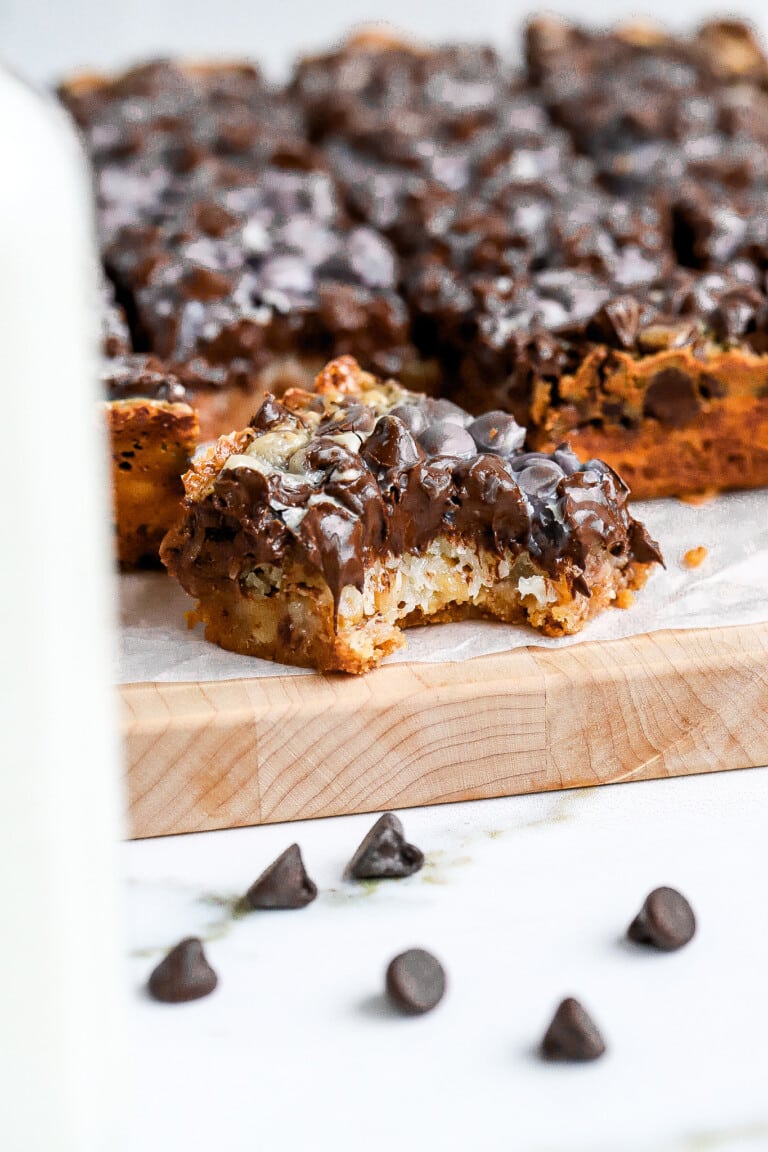 Close up shot of a bite shot of Christmas Day magic cookie bars on wooden cutting board.