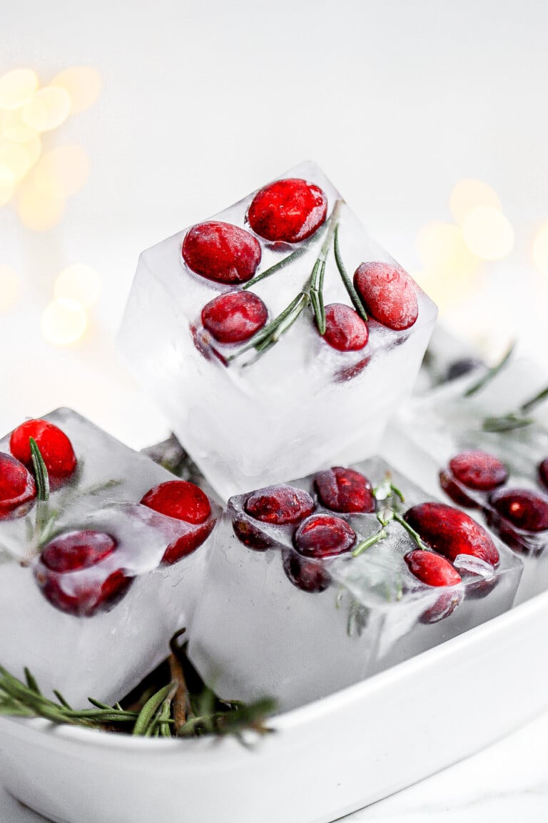 Close up shot of cranberry rosemary ice cubes with twinkle lights in background.