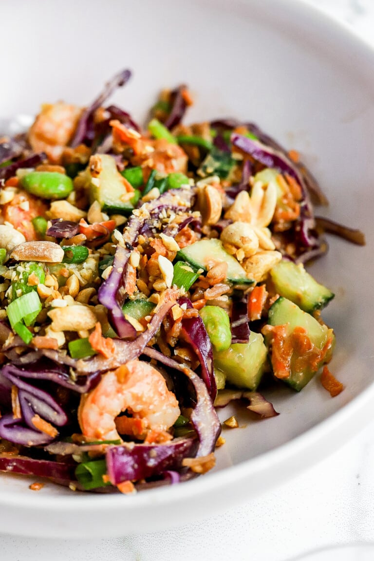 Side view of crispy rice salad in white bowl with peanut dressing and shrimp.