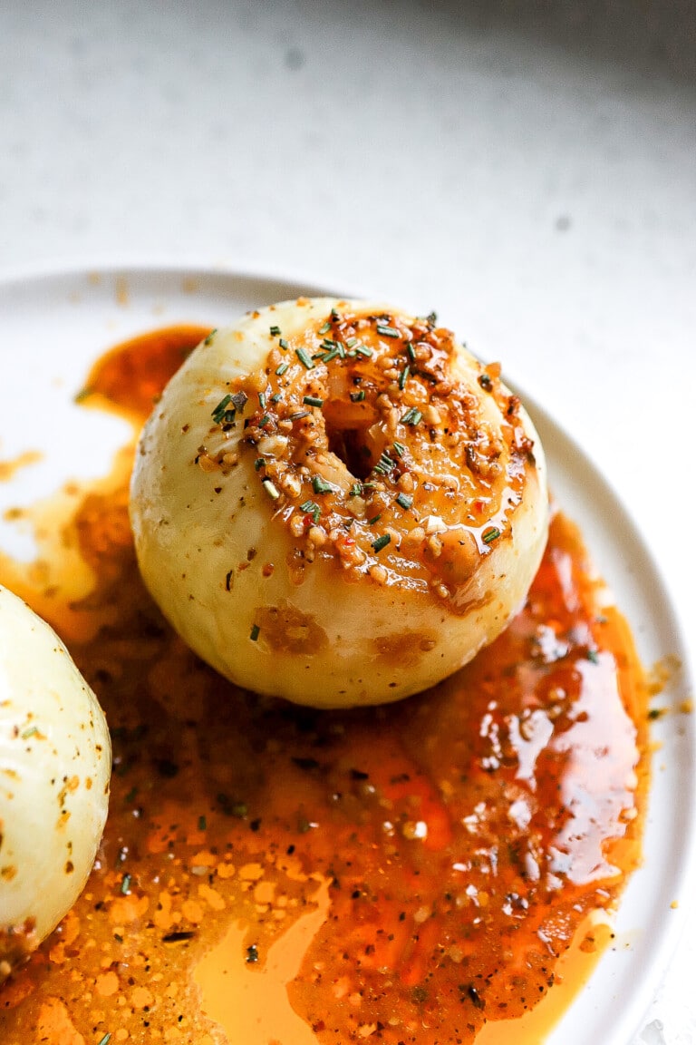 Side angle of easy onion boil with spices and butter on white plate.