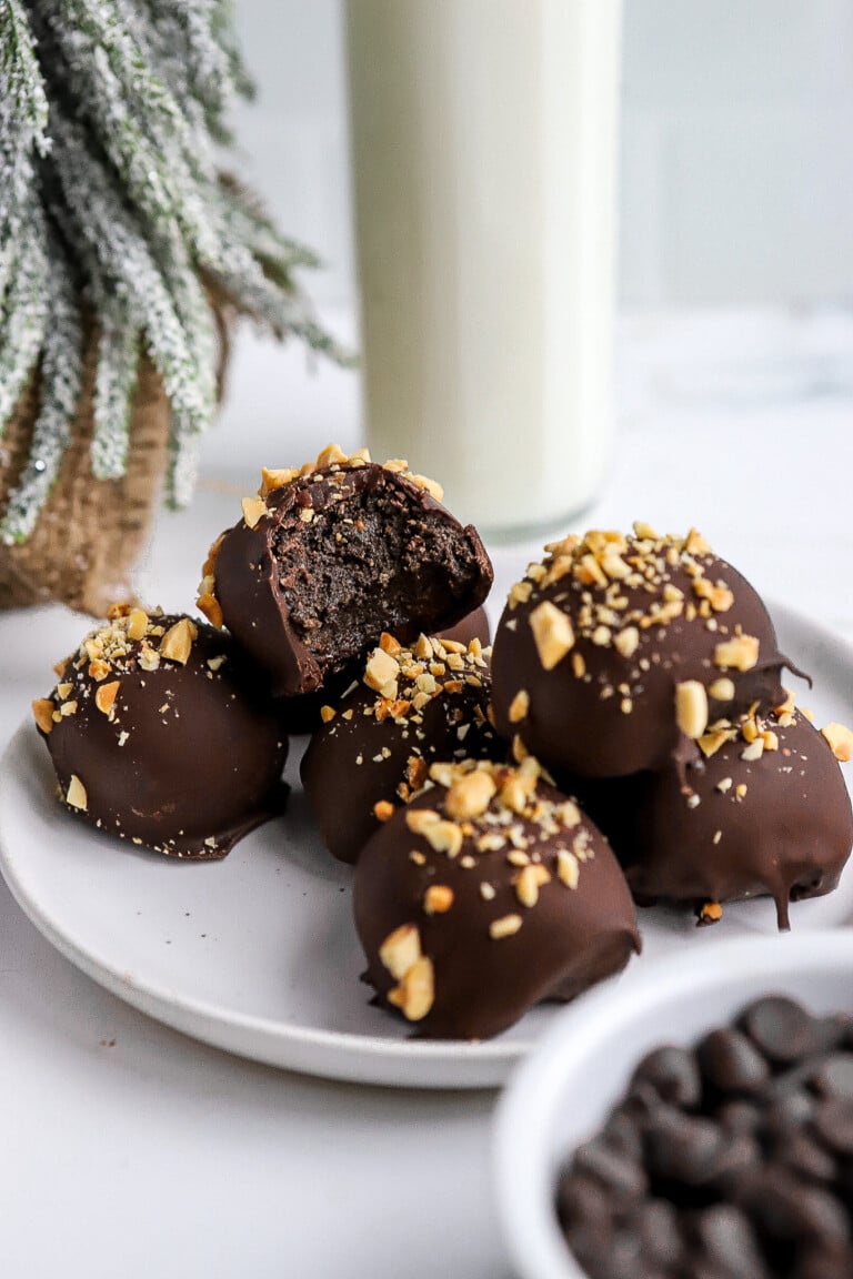 Side angle of easy oreo peanut butter balls on white plate with peanuts on top.