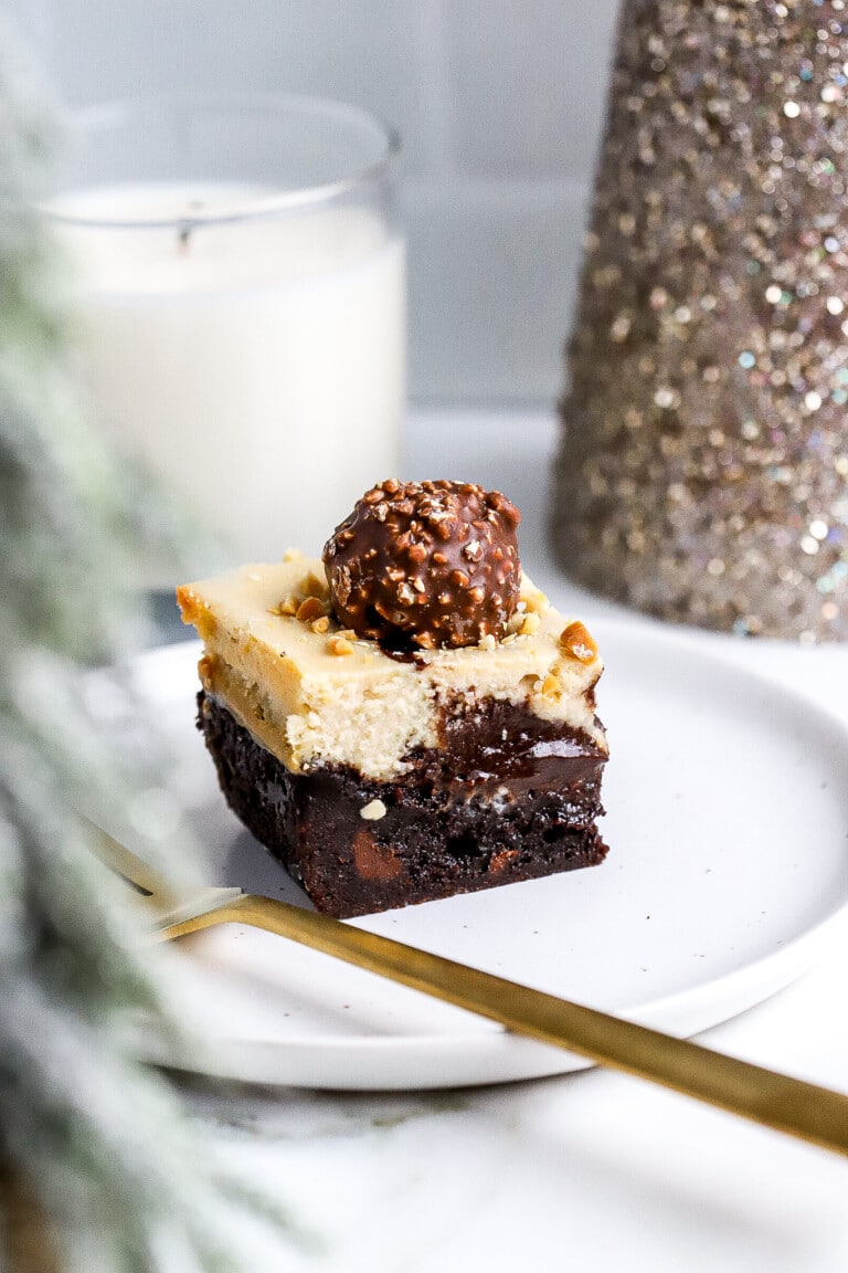 Side view of Ferrero Rocher cheesecake brownie bites on white plate with gold fork.