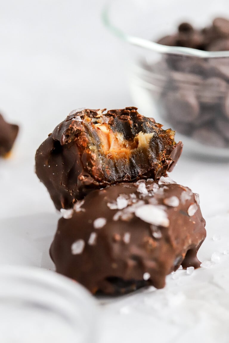 Close up shot of a date sitting on top of one another stuffed with peanut butter and topped with coarse salt on top.