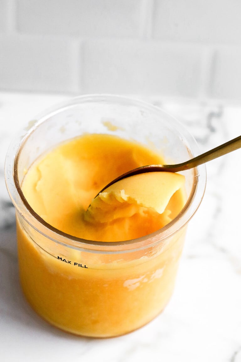 Side angle of homemade peach sorbet in ninja creami pint container with gold spoon in it.