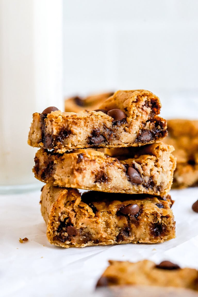 Close up shot of 3 chickpea blondies stacked on top of one another with glass of milk in background.