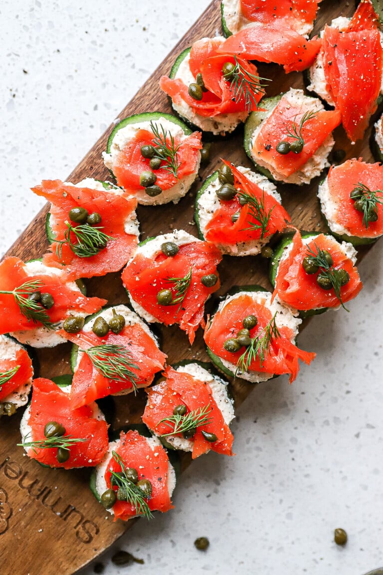 Top down view of dairy-free smoked salmon cucumber bites on wooden serving board.