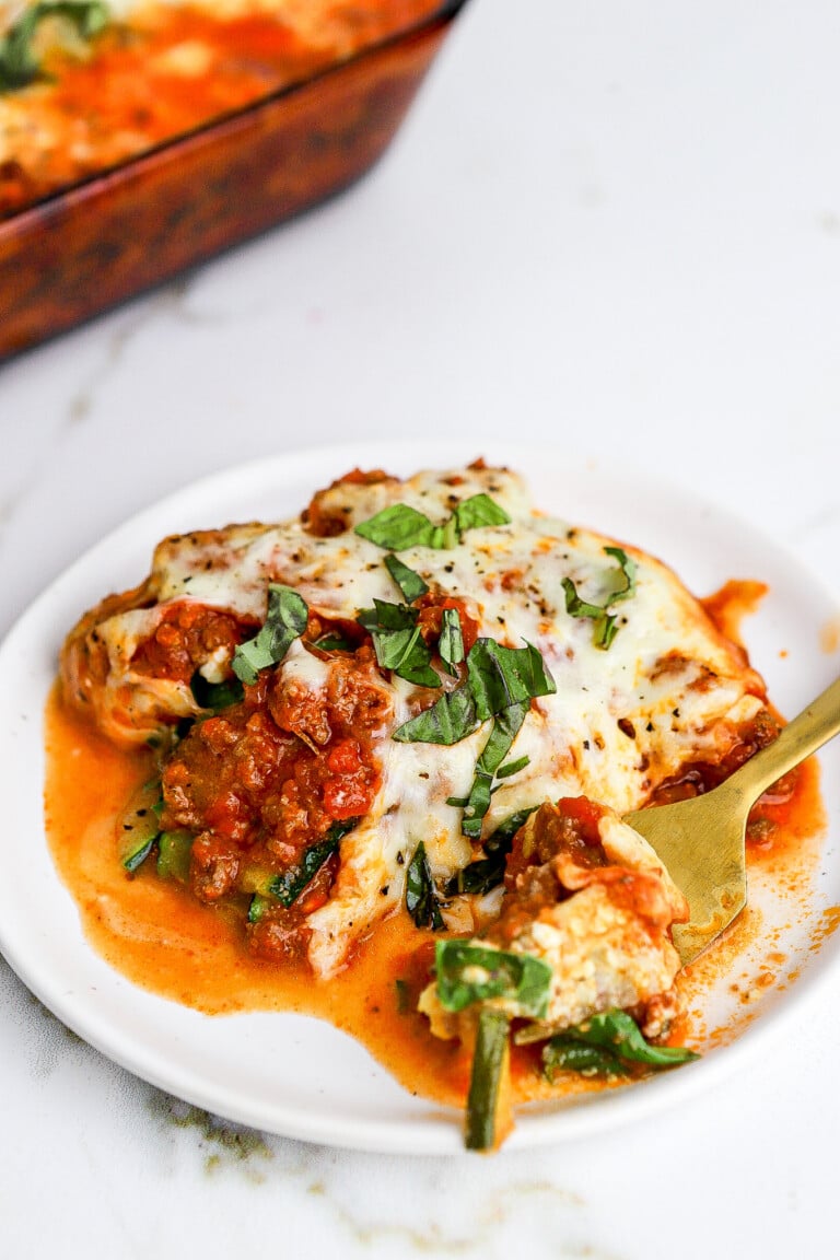 Side view of zucchini lasagna on a small white plate with a gold fork.