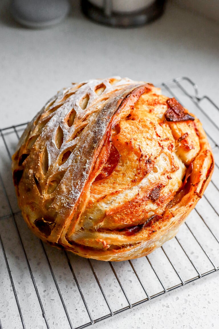 Side angle of pepperoni pizza sourdough bread on cooling rack with designs on the top of the loaf.