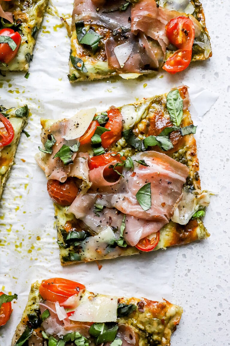 Top down view of easy chicken pesto pizza slice with fresh cherry tomatoes and prosciutto.