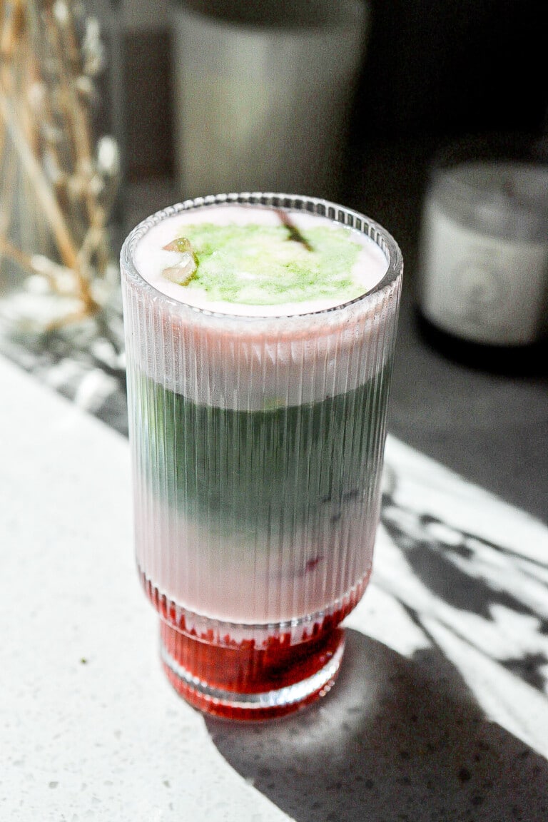 Side view of an iced protein matcha latte in a glass on white kitchen countertop.