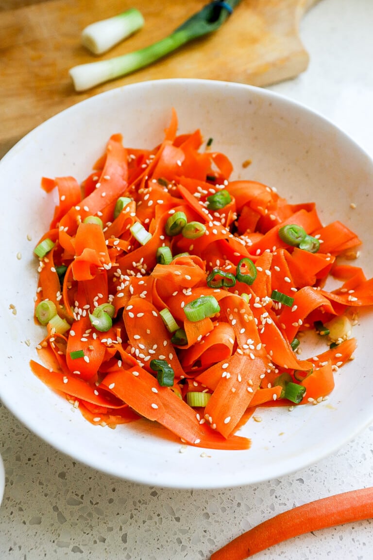 Side view of viral shaved carrot salad in white bowl with green onions and sesame seeds.