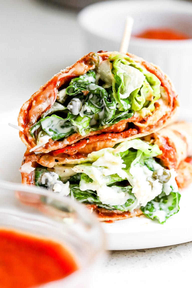 Close up shot of caesar salad pepperoni pizza wraps stacked on top of one another on white plate.