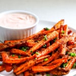 Side angle of air fryer carrot fries with sriracha mayo in background.