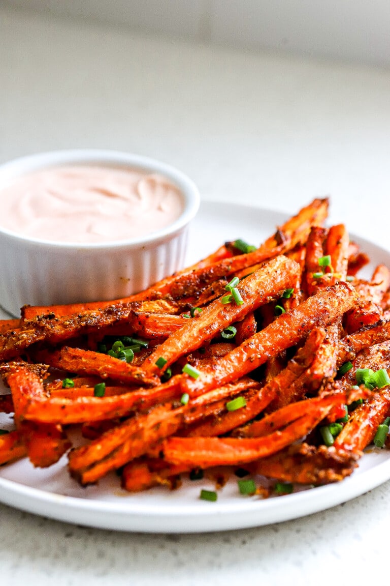 Side angle of air fryer carrot fries with sriracha mayo in background.