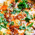 Side angle of frozen dumplings with red curry, cilantro, chili onion crisp all in one pan.