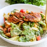 Side angle of a bowl of salad with chicken breast on top.