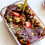 Side angle of dubai chocolate overnight oats in glass container with gold spoon.