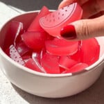Side angle of a hand picking up a sour watermelon candy with red fingernails.