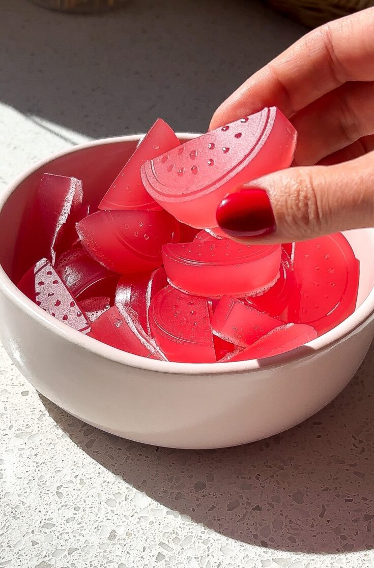 Side angle of a hand picking up a sour watermelon candy with red fingernails.