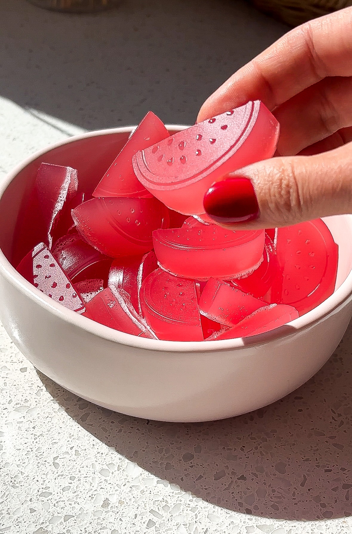 Side angle of a hand picking up a sour watermelon candy with red fingernails.