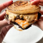 Hands holding a high protein burger with white plate in background.
