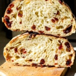 Close up shot of cranberry sourdough stacked on top of one another on wooden cutting board.