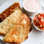 Top down view of 3 crispy tacos with chiptole sauce and pico de gallo in small containers.