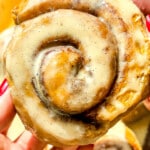 Protein cream cheese icing spread over warm pumpkin cinnamon roll in human hands