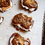 Smashed date s'mores on parchment topped with melted chocolate and crushed graham crackers